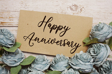Happy Anniversary text on paper card with rose flowers bouquet on wooden background
