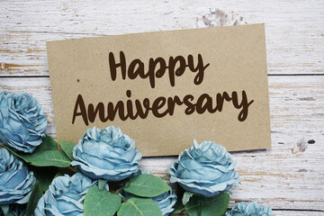Happy Anniversary text on paper card with rose flowers bouquet on wooden background