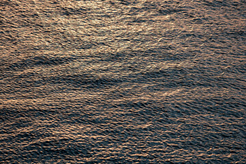 Small waves gently rippling across a water surface, reflecting the warm golden hues of a stunning sunset, creating a serene atmosphere