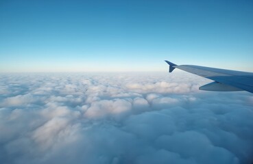 Fototapeta premium Aerial view of airplane with blue wing, tail against light blue sky. Perspective from below creates sense of scale, distance. Norway landscape below, mountains, sea, snow-capped peaks visible from