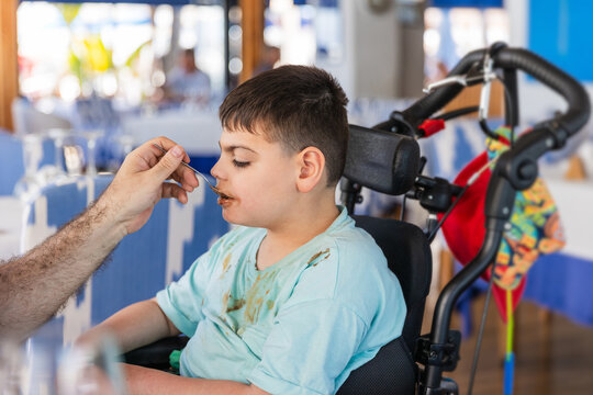 Father feeding disabled son in wheelchair at restaurant