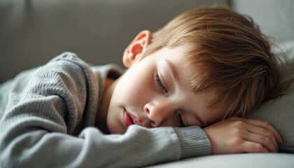 Young boy sleeps peacefully with eyes closed. Golden hair boy lies on his side in gray sweatshirt. Casual and comfortable vibe with simple gray background.