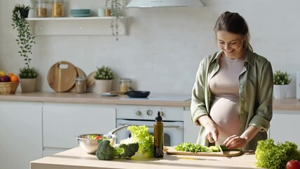 positive pregnant young woman cutting vegetables for salad in kitchen, healthy food concept