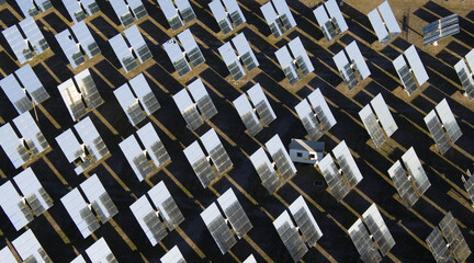 Aerial view of shimmering solar mirrors stretch across the arid landscape, reflecting the bright sky and casting dark shadows, AlmerÃ­a, Andalusia, Spain.
