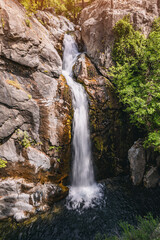 Stunning waterfall flows down a rugged cliff surrounded by lush greenery, creating a serene and captivating natural landscape