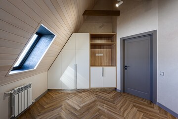 Attic room featuring sloped ceiling, a window, closet, wooden floors laid in a herringbone pattern...