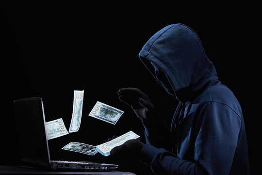A masked hacker with a laptop fraudulently steals money through the Internet. The concept of security of bank credit cards and online transfers. Cybercrime.