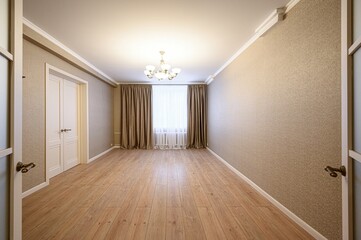 Empty room with wood floors, beige textured walls, a window with curtains, and a chandelier. Doors are slightly ajar