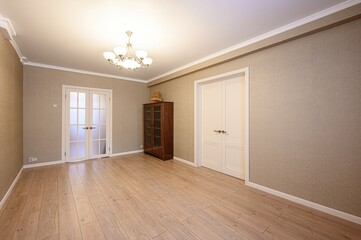 An empty room with beige walls, wooden floors, and white trim. A glass cabinet sits against one...