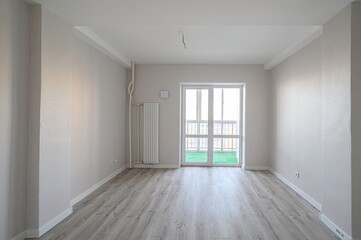 Obraz premium bright, empty room with light gray walls, wood-look floors, and a white door leading to a balcony. Minimalist design
