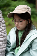 Sad girl in baseball cap, glasses, and raincoat sitting beside her grandmother on a park bench....