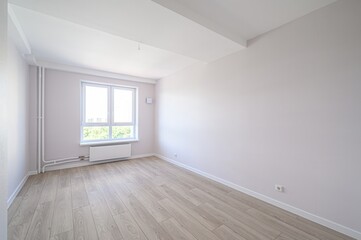 Bright, empty room with light wood flooring, white walls and ceiling, and a window offering an outside view. Clean and modern