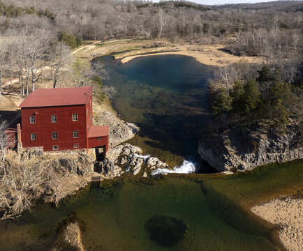 Aerial view of the stark red mill house contrasting against the clear blue waters of the spring, surrounded by the raw, untamed landscape, Missouri, United States.