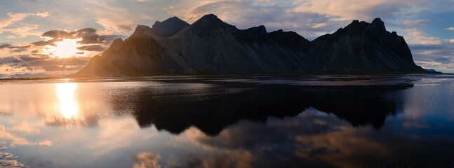 Golden light casts a warm glow on Vestrahorn mountain in Stokksnes, Iceland, enhancing its dramatic...