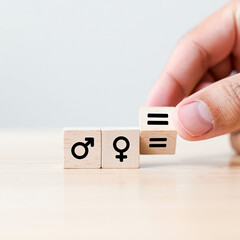 Hand placing wooden cube with equal sign between male and female symbols