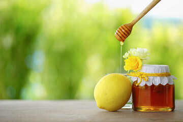 Honey in a glass jar and lemon with green background