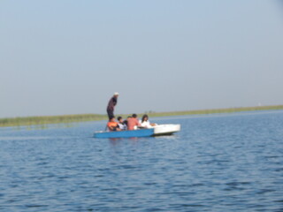 A man paddles his boat on the serene water, enjoying a summer day of fishing and nature