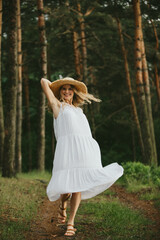 Happy woman wearing white dress and straw hat enjoying nature in forest