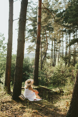 Woman wearing white dress and straw hat relaxing in sunny forest