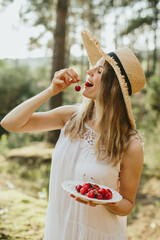 Woman eating cherries in nature holding plate and smiling