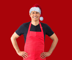 Studio shot of a man with red apron and positive emotions while wearing a Christmas hat against a...