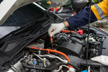 Mechanic checking car engine oil level with dipstick in vehicle engine bay