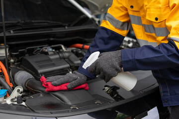 Fototapeta premium Mechanic cleaning car engine with spray and cloth, wearing gloves and safety jacket