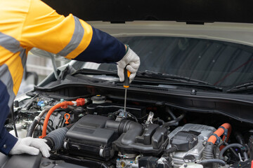Mechanic in uniform inspects car engine with screwdriver