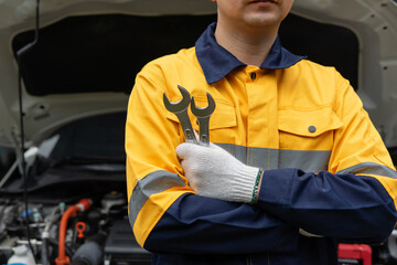 Mechanic in yellow uniform holding wrenches in front of car engine
