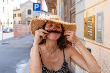 a beautiful smiling middle-aged woman wearing a straw hat having fun playing with her hair on a...
