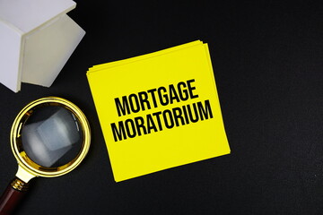 Mortgage Moratorium text message with white house model and magnifying glass top view on black...