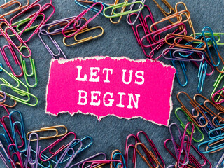 Let us begin message written on ripped torn pink paper piece on grey background. Conceptual let us...