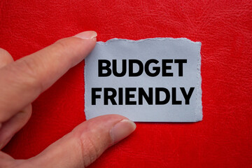 Budget friendly message written on ripped torn grey paper piece on red background. Conceptual...