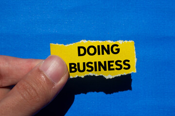 Doing business message written on ripped torn yellow paper piece on blue background. Conceptual doing business symbol. Copy space.