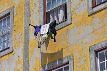 Yellow paint peeling off from plaster facade of weathered town house with laundry hanging in front of window. Location: Porto Portugal