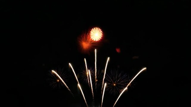 Fireworks in slow motion exploding against dark night sky, colorful bursts with light trails and sparkles creating festive celebratory atmosphere, no people