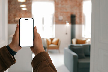 Person holding smartphone with blank screen in cozy loft interior with mustard armchairs, gray...