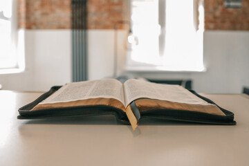 Open Bible placed on table in cozy loft-style living room with brick wall and soft lighting....