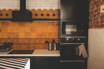 Modern kitchen with black appliances, beige and terracotta tiles, and vintage ceramic pattern. Oven...