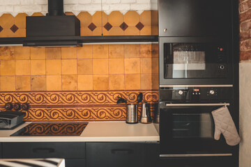 Modern kitchen with black appliances, beige and terracotta tiles, and vintage ceramic pattern. Oven...