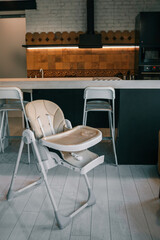 Modern baby high chair in stylish kitchen interior with bar stools, pendant lights, and patterned tiles. Cozy mix of industrial and homey design elements