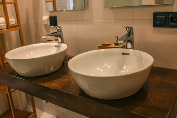 Modern white ceramic washbasins with chrome faucets on wooden countertop in a stylish bathroom interior