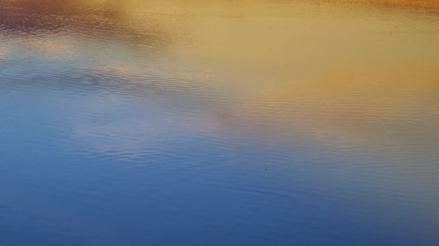 Soft golden and orange tones linger on the sea surface just after the sun dips below the horizon&mdash;handheld framing reveals slight motion in water ripples and light reflections, evoking warmth, imperman