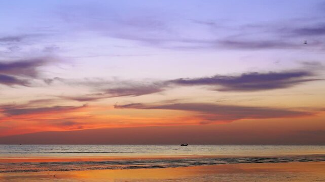 As the golden sunset fades into a warm-hued sky, distant boats linger near the horizon while birds glide gracefully through the evening air&mdash;gentle ripples shimmer across the water, evoking a tranquil 