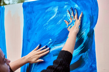 Young female with fair hair, engaging in expressive painting using hands. Dynamic blue strokes...