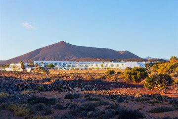 Modern white hotel stands out against volcanic mountains and arid landscape in the Canary Islands, bathed in warm sunlight. Ideal for travel, nature, tourism, or resort-themed visual projects