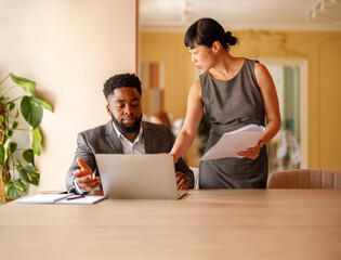 Serious financial professionals analyzing reports over laptop while working together at office desk
