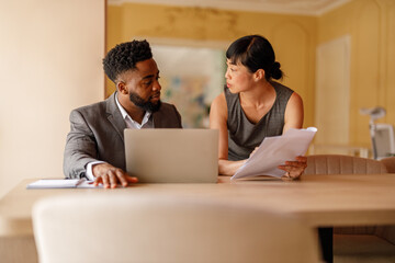 Focused business professionals discussing project with documents and laptop and sharing ideas in...