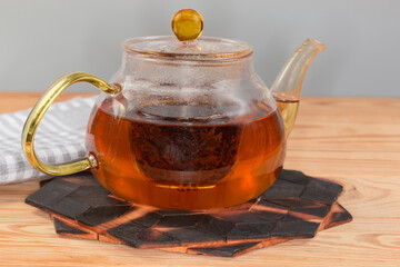 Steeped black tea in glass teapot on stand, side view
