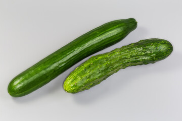 Two whole long cucumbers of different varieties on gray background